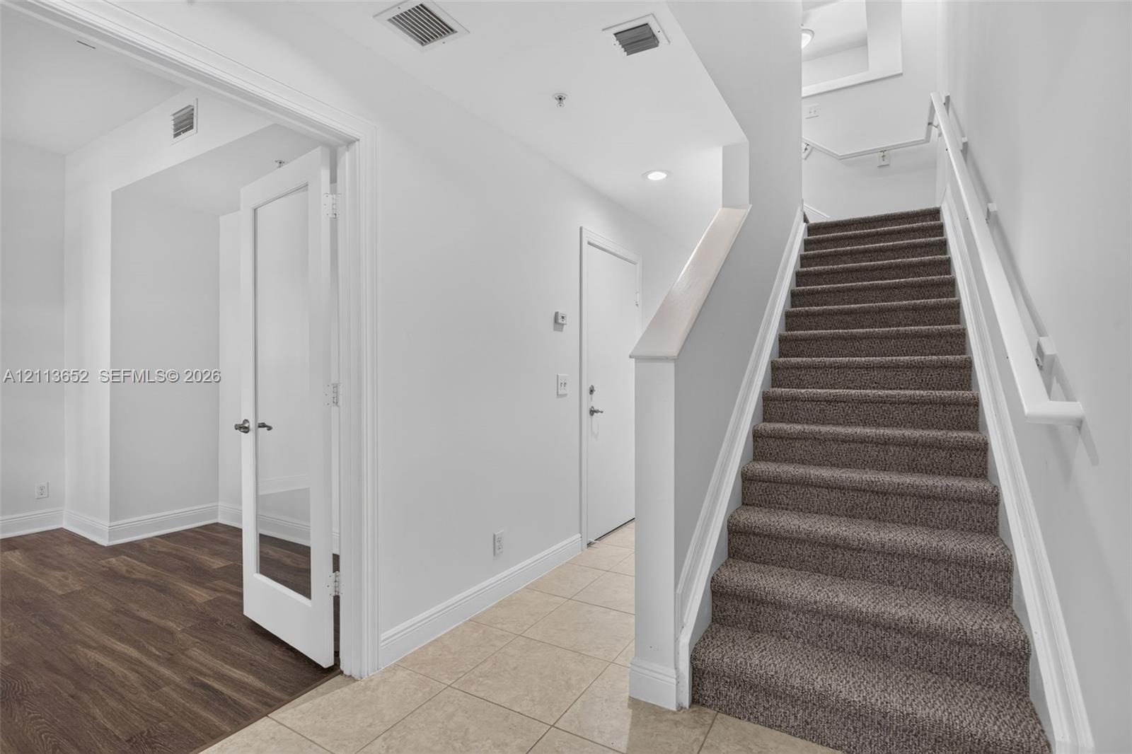 Foyer featuring neutral tile flooring, staircase with carpeted treads, and a glass-panel interior door opening to wood-finish flooring