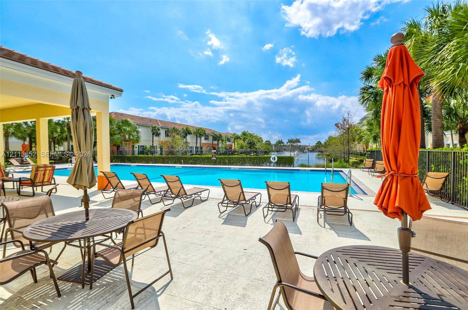 Community swimming pool featuring a concrete deck, covered patio area, metal fencing, and water frontage