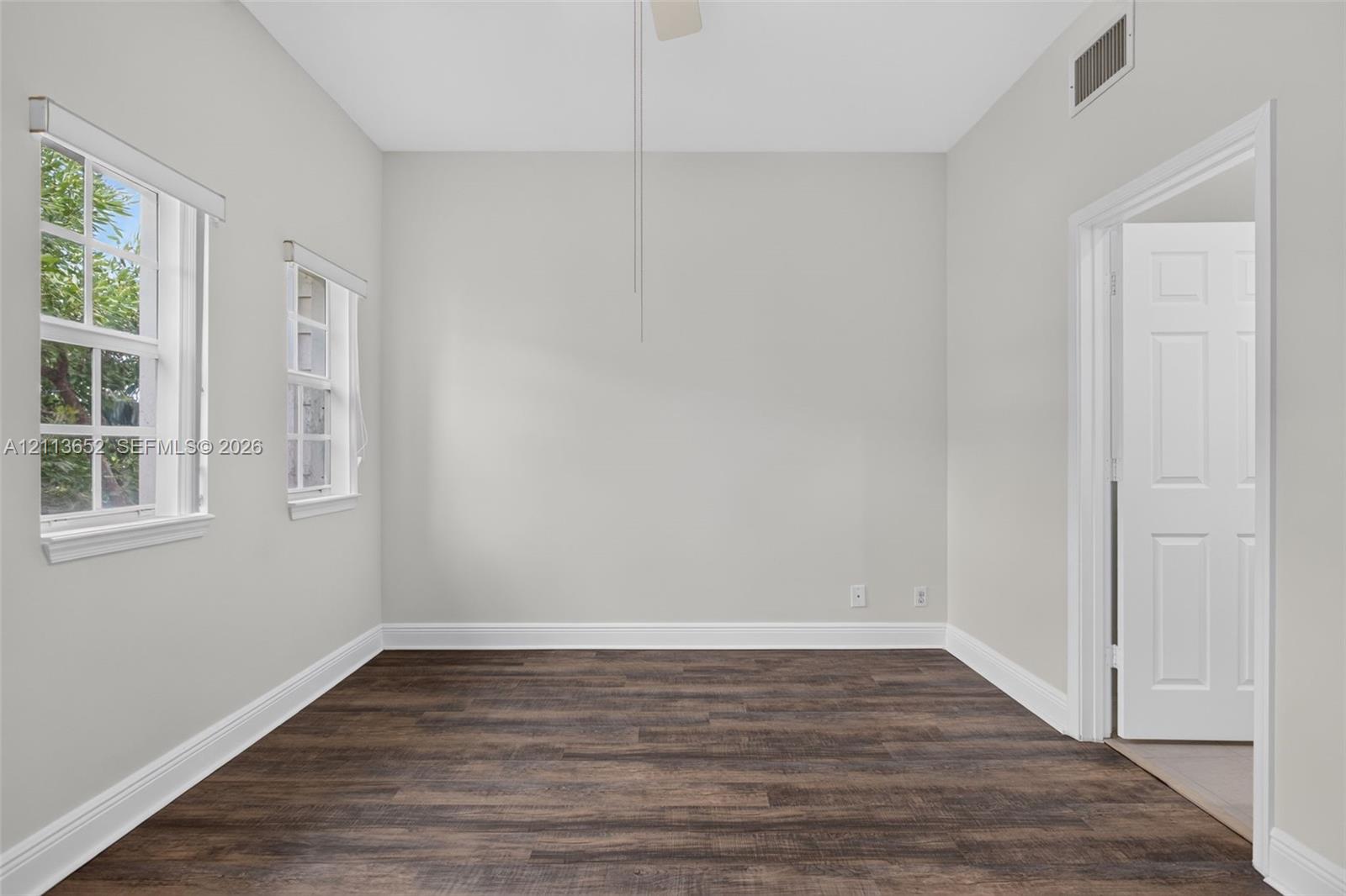 Room featuring wood-finish flooring, neutral wall paint, two multi-pane windows, and a classic six-panel door
