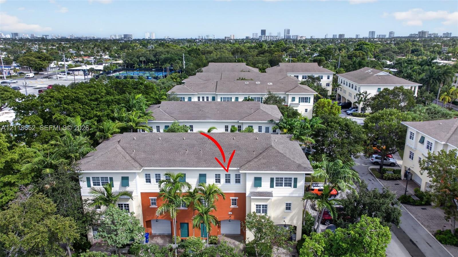 Multi-story townhouse exterior featuring a high-contrast stucco facade, attached garage, shingled hip roof, and surrounding mature landscaping