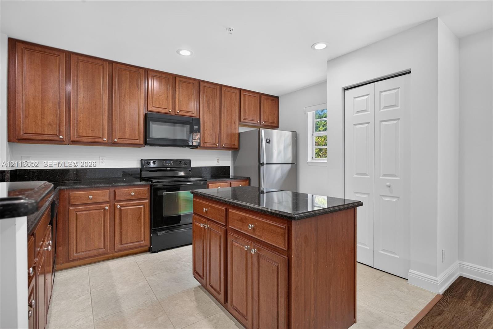 Kitchen featuring wood cabinetry, stone-surface countertops, central island, stainless steel appliances, and tile flooring