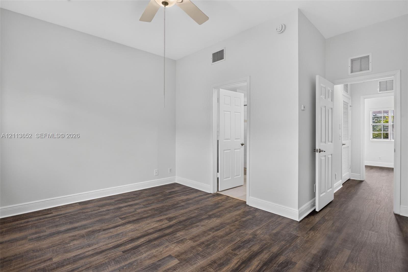 Interior room featuring wood-finish flooring, neutral wall paint, a ceiling fan, and multiple six-panel interior doors