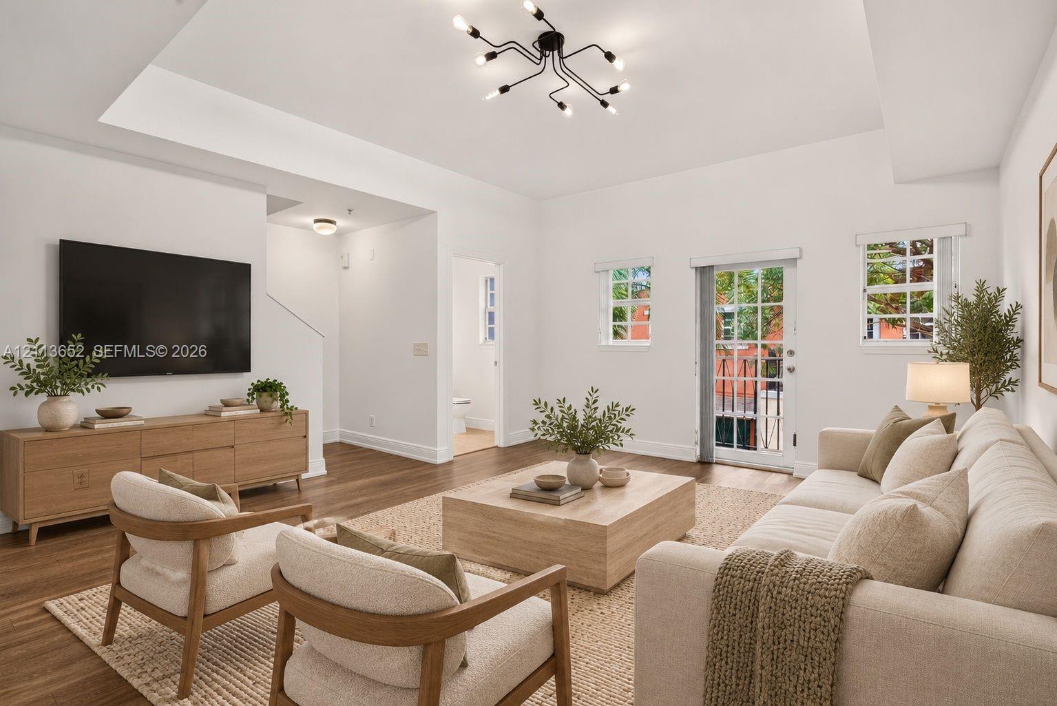 Living area featuring a tray ceiling, wood-finish flooring, multi-arm sputnik lighting fixture, and a glass-paneled exterior door