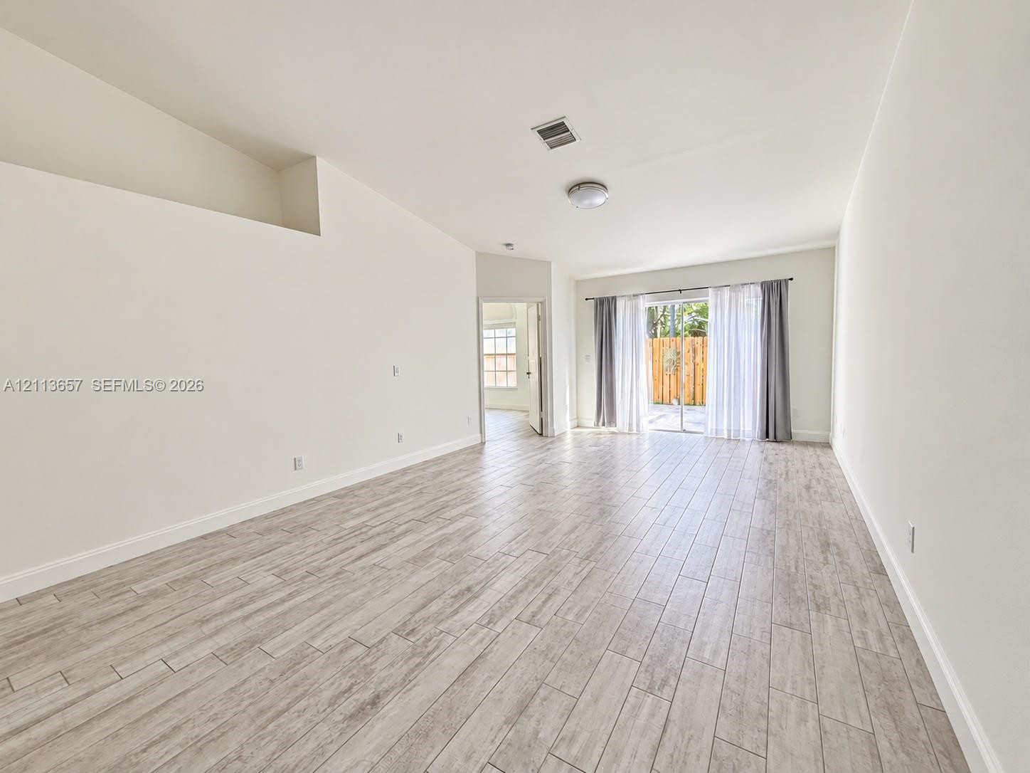 Open-concept room featuring vaulted ceilings, wood-finish tile flooring, and sliding glass doors Open-concept room featuring vaulted ceilings, wood-finish tile flooring, and sliding glass doors
