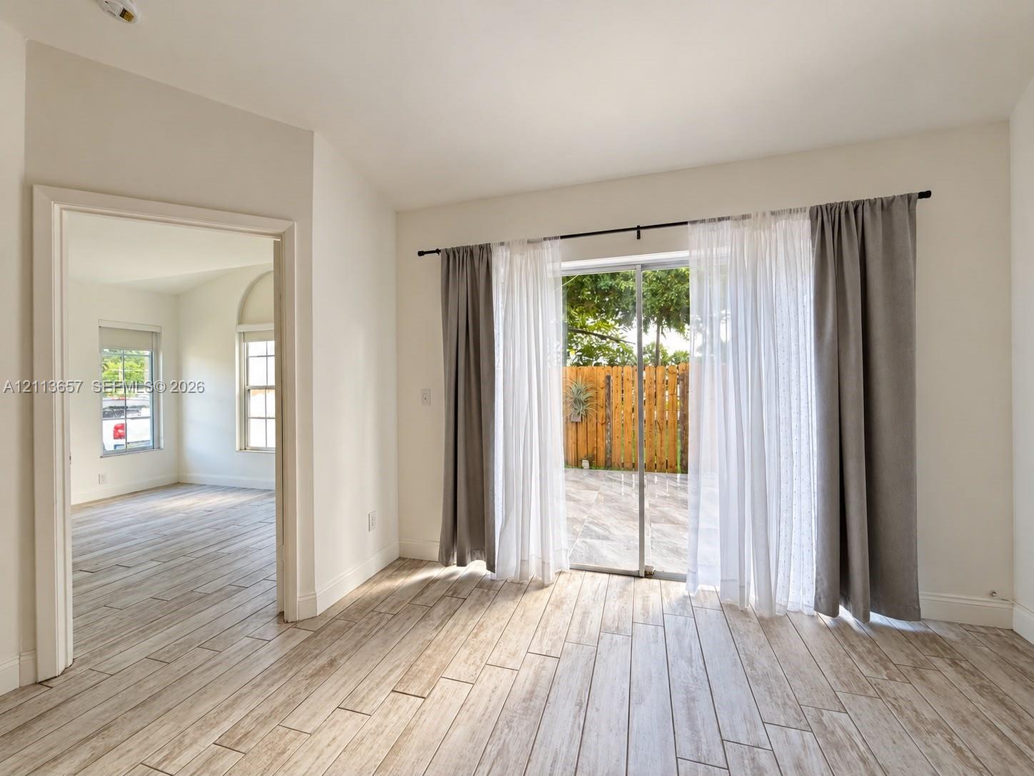 Wood-finish tile flooring throughout, neutral interior paint, and sliding glass doors with exterior access to a paved patio Wood-finish tile flooring throughout, neutral interior paint, and sliding glass doors with exterior access to a paved patio