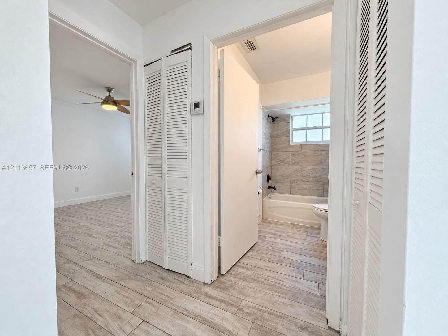 Wood-finish flooring throughout, louvered closet doors, and a bathroom featuring full-height stone-finish wall tile, a built-in shower-tub combination, and matte black hardware Wood-finish flooring throughout, louvered closet doors, and a bathroom featuring full-height stone-finish wall tile, a built-in shower-tub combination, and matte black hardware