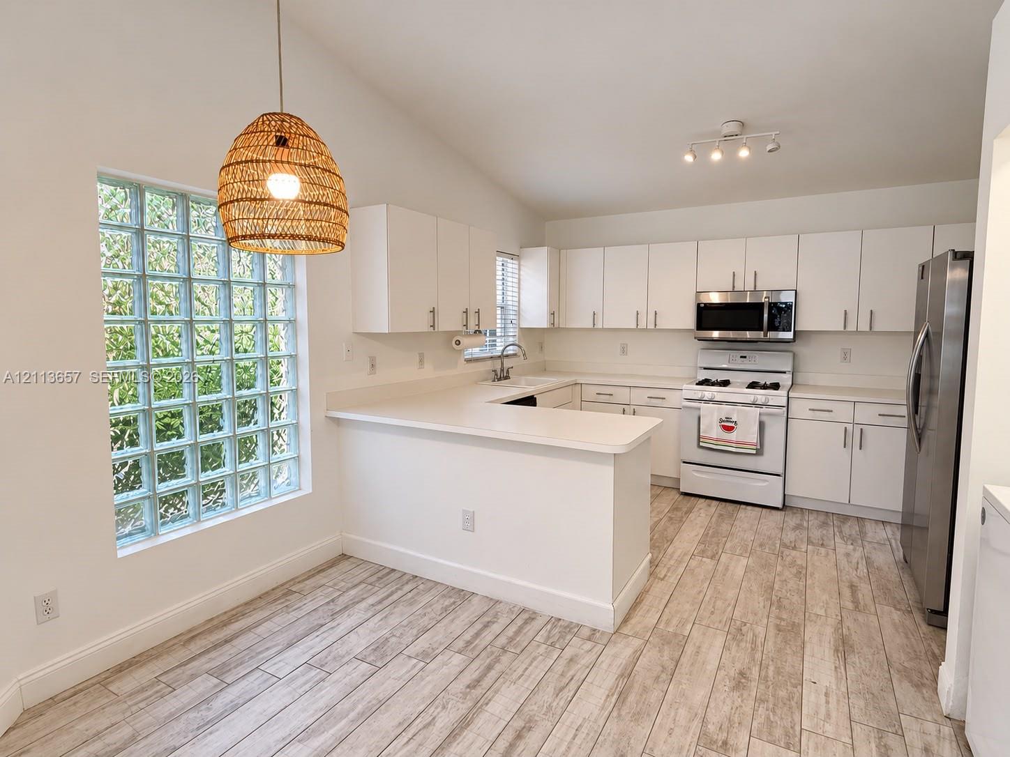 Kitchen featuring white cabinetry, wood-finish flooring, glass block window, and stainless steel appliances Kitchen featuring white cabinetry, wood-finish flooring, glass block window, and stainless steel appliances