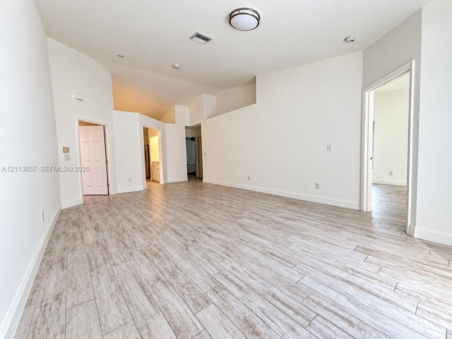 Spacious room featuring vaulted ceilings, neutral wall tones, and wood-finish tile flooring