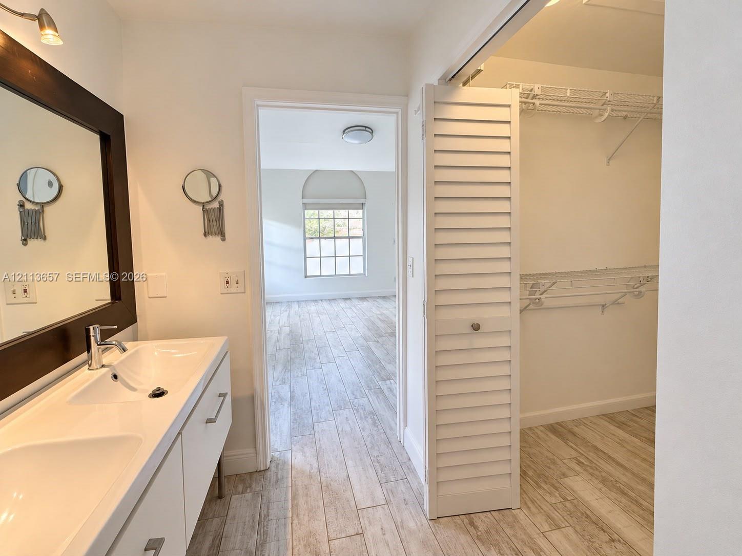 Bathroom vanity with dual integrated sinks, wood-finish tile flooring, and louvered bifold closet doors Bathroom vanity with dual integrated sinks, wood-finish tile flooring, and louvered bifold closet doors