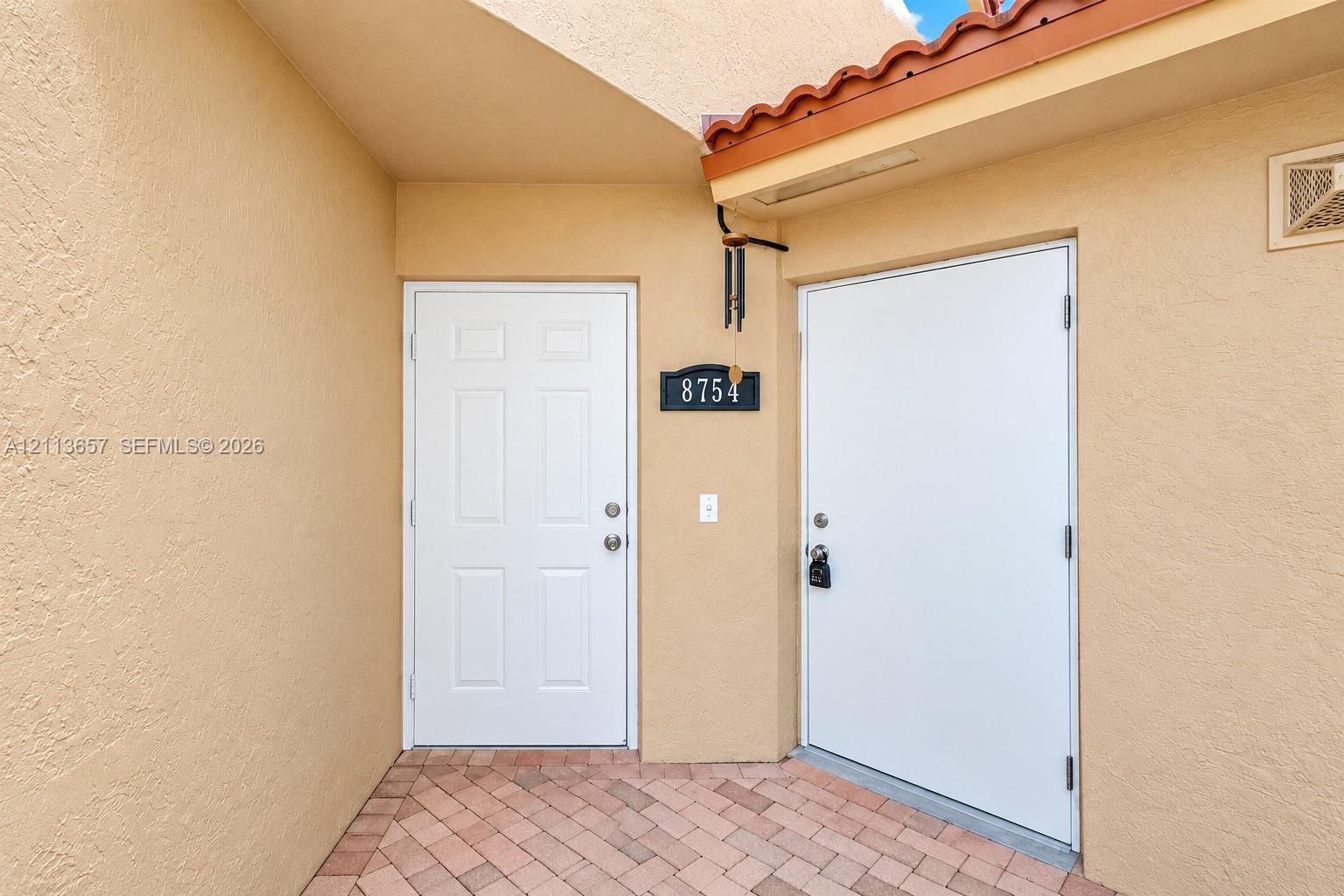 Stucco exterior entry featuring a brick-paver walkway, recessed entryway, and clay-tile roof trim