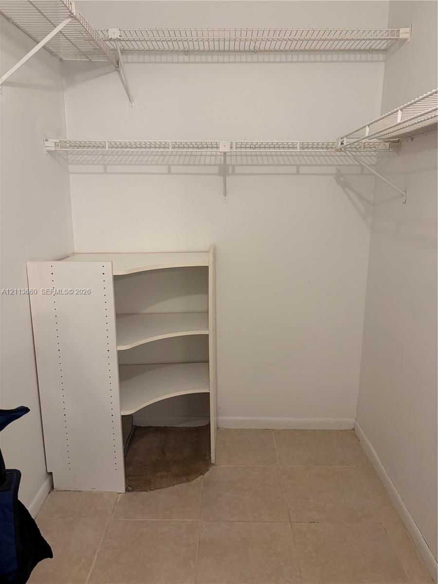 Walk-in closet featuring dual-tier wire shelving and built-in corner storage unit with tile flooring