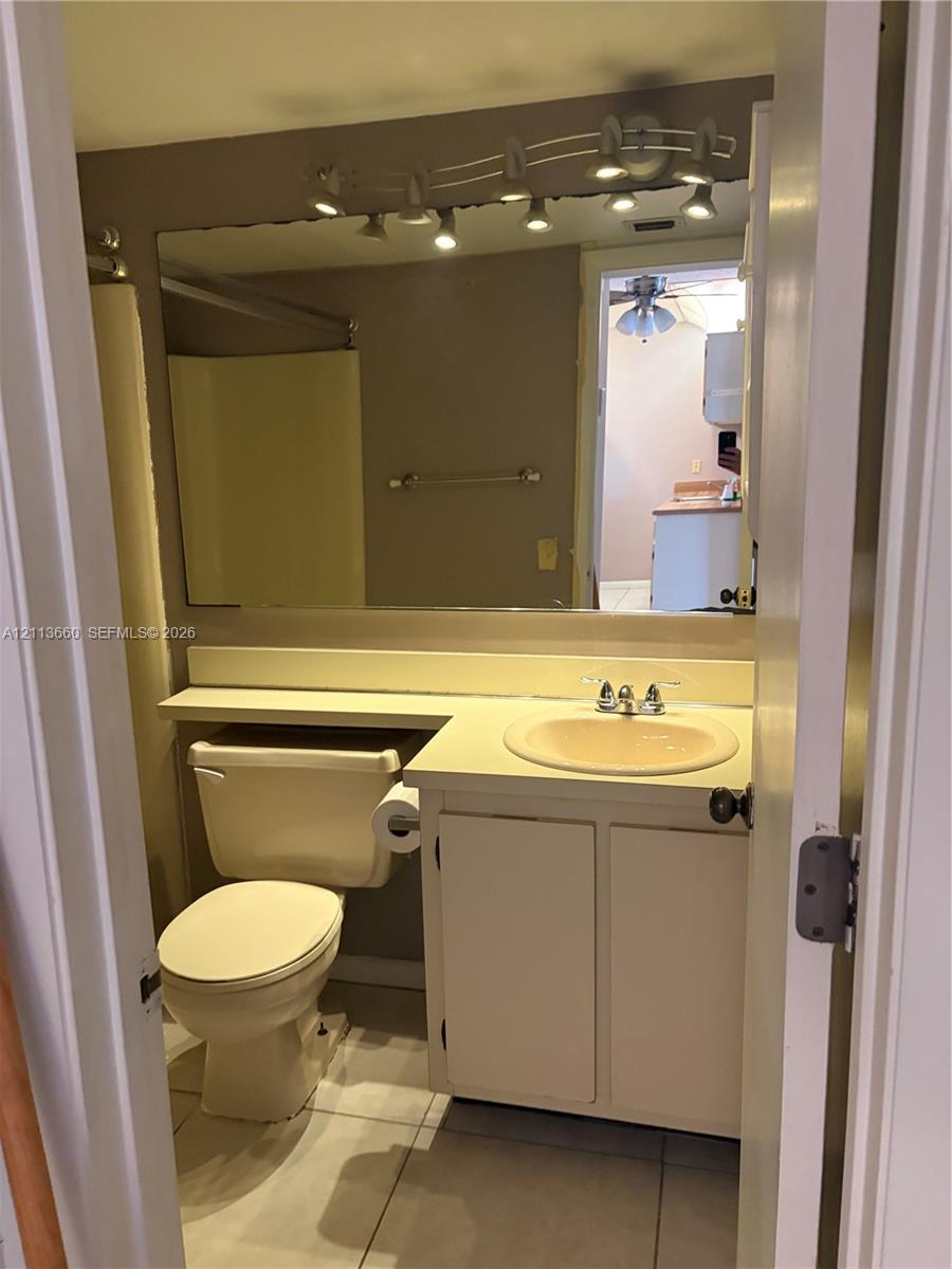 Bathroom featuring a vanity with integrated sink and countertop, large wall-mounted mirror, multi-bulb track lighting, and tile flooring