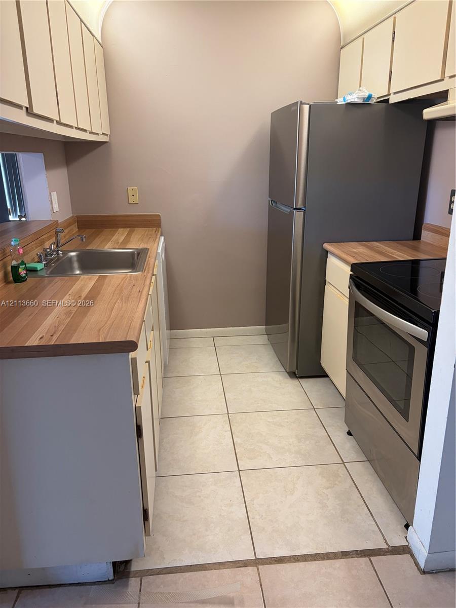 Kitchen featuring wood-finish countertops, stainless steel appliances, ceramic tile flooring, and light-toned upper and lower cabinetry