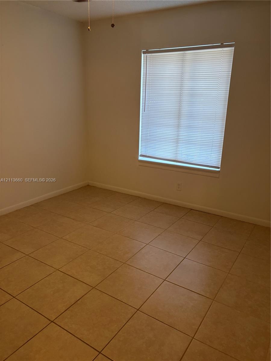Neutral-toned ceramic tile flooring, clean painted walls, single window with integrated horizontal blinds, and a ceiling fan fixture