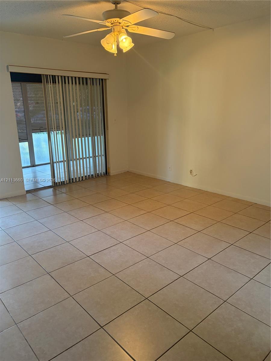 Neutral-toned tile flooring, ceiling fan with integrated lighting, and sliding glass doors featuring vertical blinds