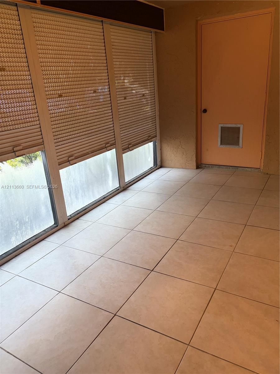 Enclosed patio featuring large-format tile flooring and multiple windows equipped with exterior-mounted manual security shutters