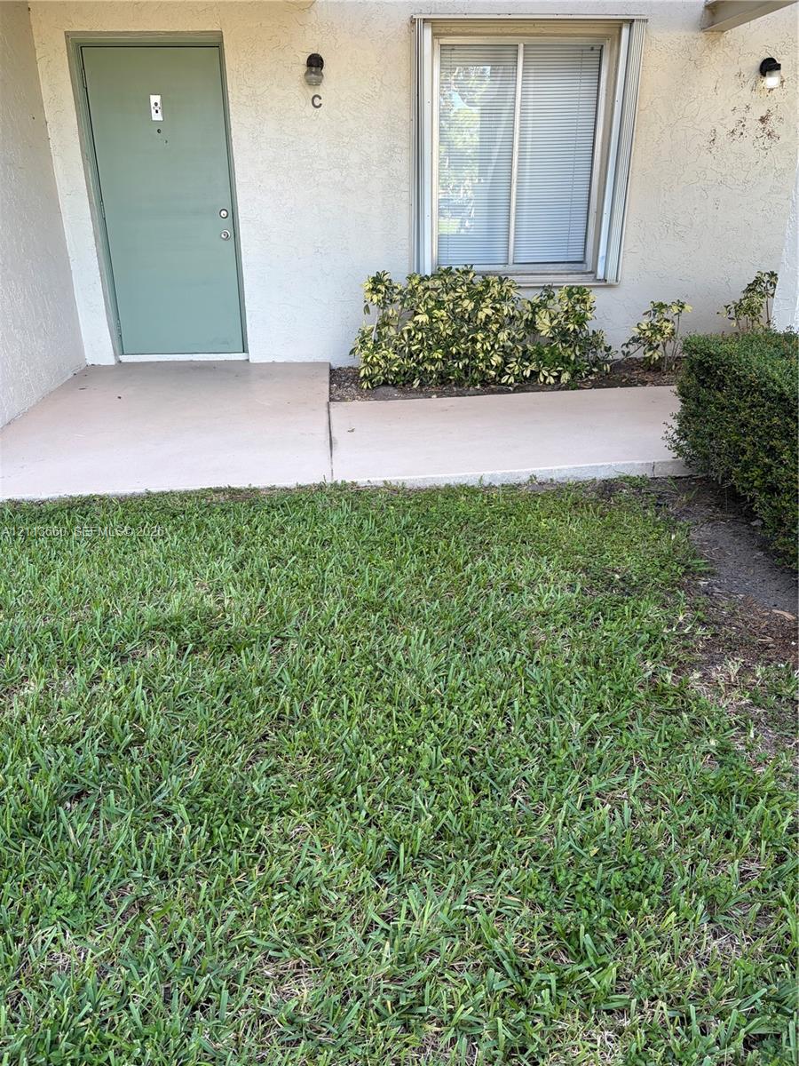 Exterior entrance featuring a concrete walkway, stucco siding, and installed wall-mounted light fixtures