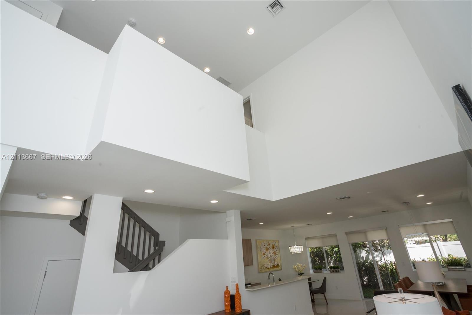 Double-height volume ceiling, recessed lighting, and staircase with dark-toned balustrades Double-height volume ceiling, recessed lighting, and staircase with dark-toned balustrades