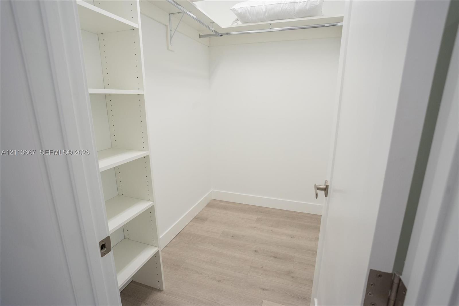 Walk-in closet featuring white built-in shelving, wood-finish flooring, and a metal garment rod