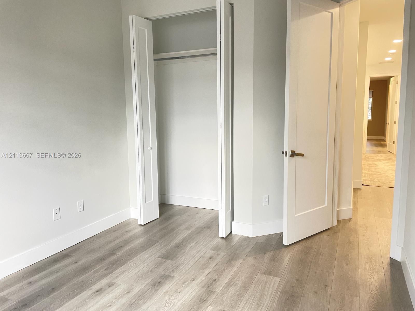 Interior room featuring wood-finish flooring, a built-in closet with double-panel doors, and a shaker-style interior door with brushed metal hardware
