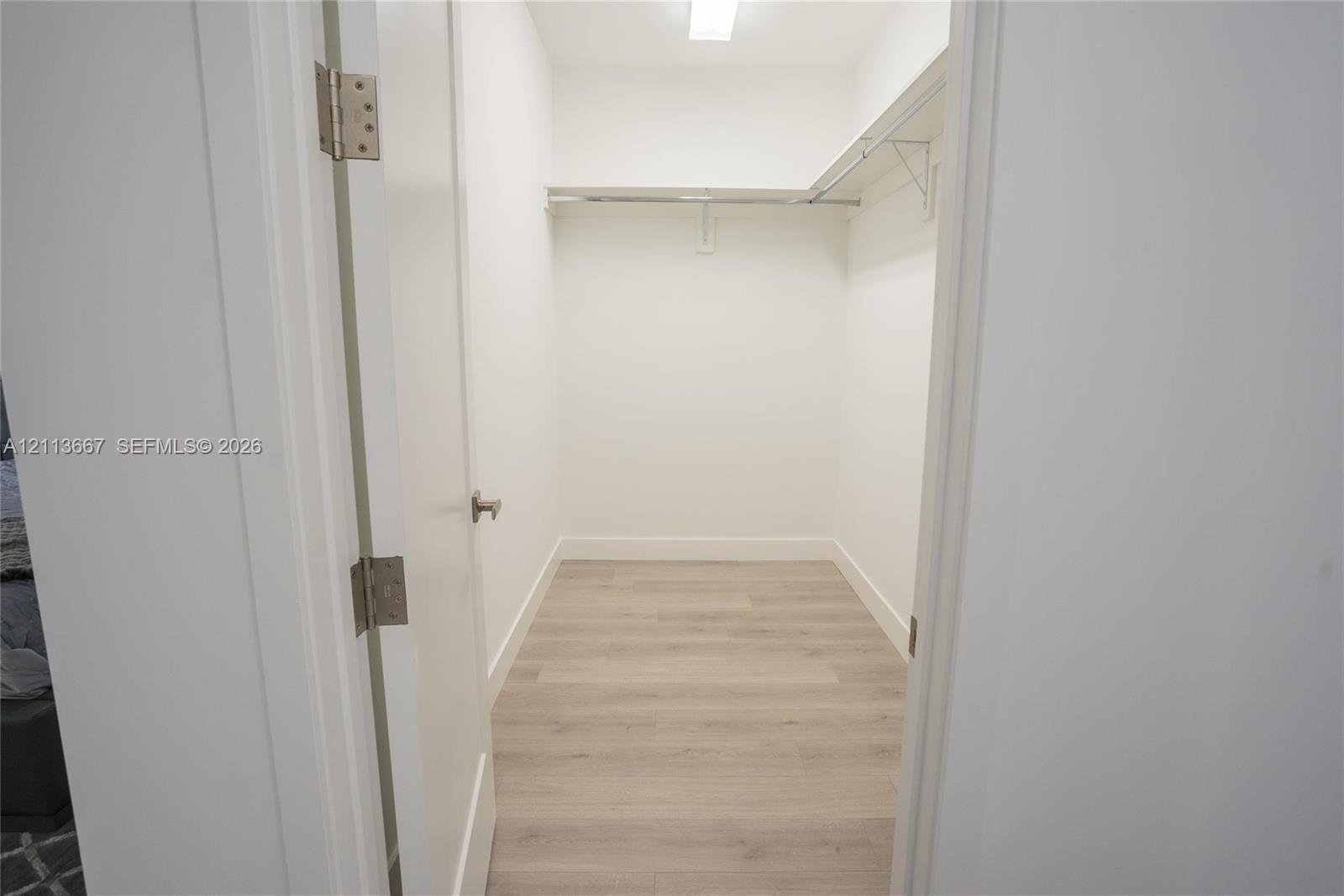 Walk-in closet featuring wood-finish flooring, white walls, and built-in shelving with an integrated clothes rod