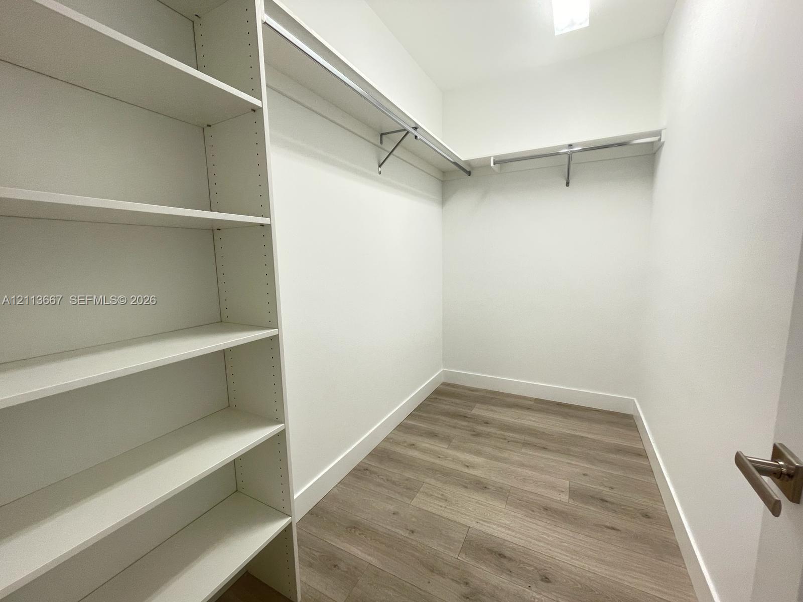 Storage area featuring white built-in shelving, metal garment rods, and wood-finish flooring