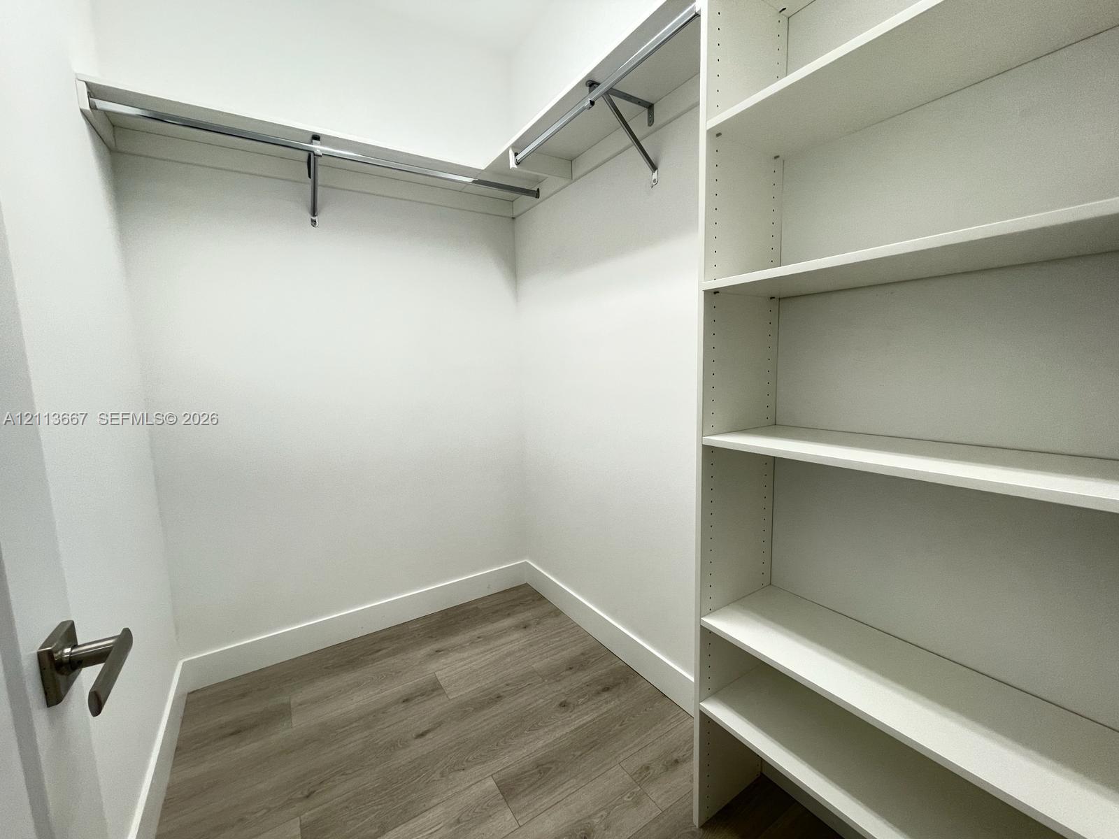 Walk-in closet featuring white built-in shelving, wood-finish flooring, and integrated metal clothing rods