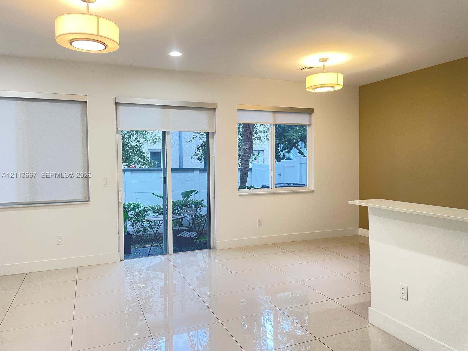 Interior space featuring large-format tile flooring, dual drum pendant lighting, a glass sliding door with integrated window shades, and a built-in counter Interior space featuring large-format tile flooring, dual drum pendant lighting, a glass sliding door with integrated window shades, and a built-in counter