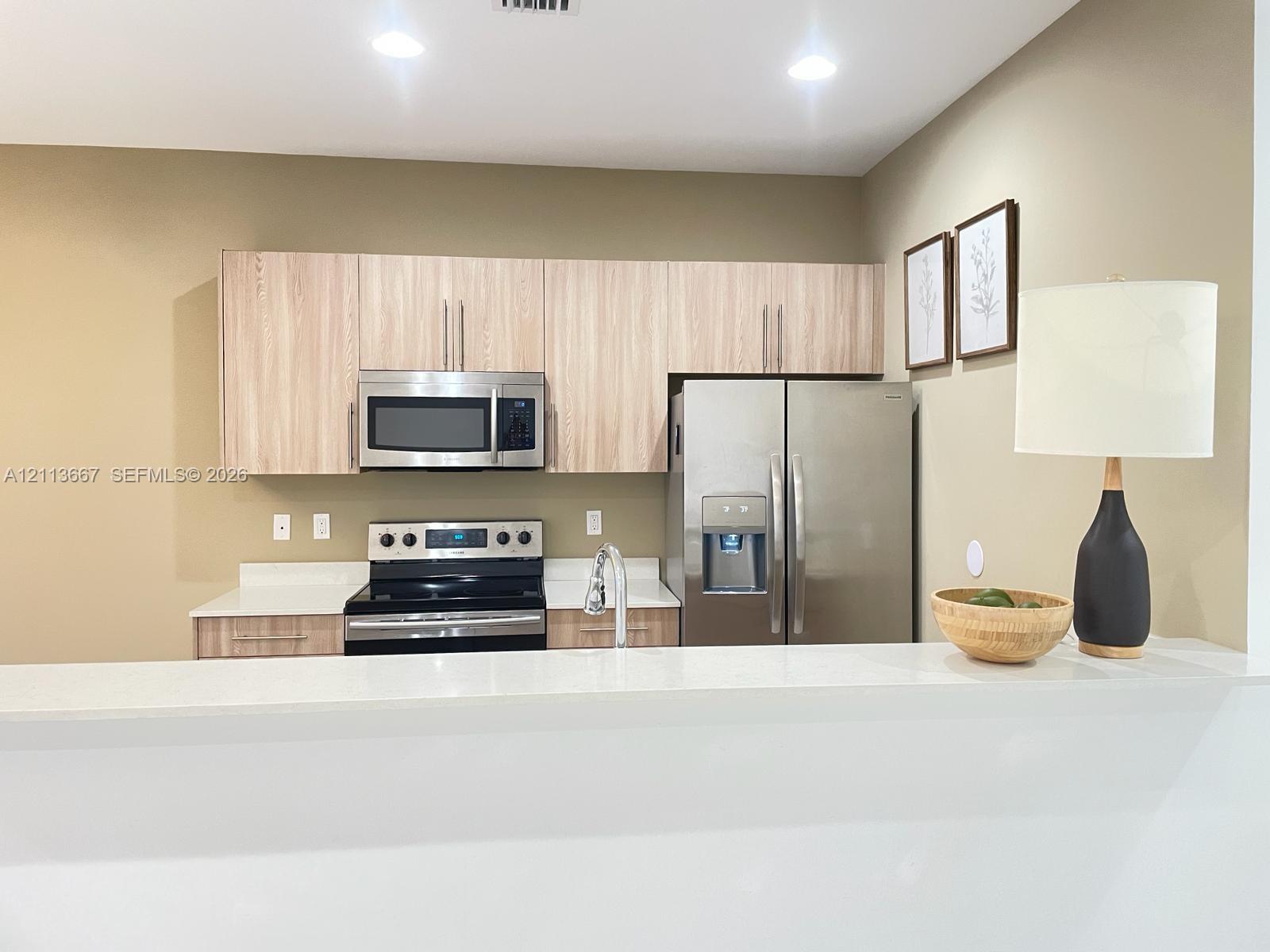 Kitchen featuring flat-panel wood-finish cabinetry, stainless steel appliances, and solid surface countertops Kitchen featuring flat-panel wood-finish cabinetry, stainless steel appliances, and solid surface countertops