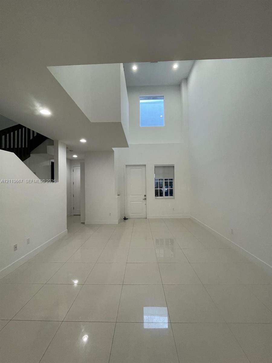 High-ceiling interior featuring glossy tile flooring, recessed lighting, and a staircase with a dark wood-finish railing High-ceiling interior featuring glossy tile flooring, recessed lighting, and a staircase with a dark wood-finish railing