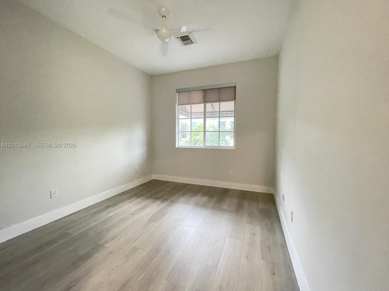 Neutral-toned interior featuring wood-finish flooring, a multi-pane window with a roller shade, and a ceiling-mounted fan