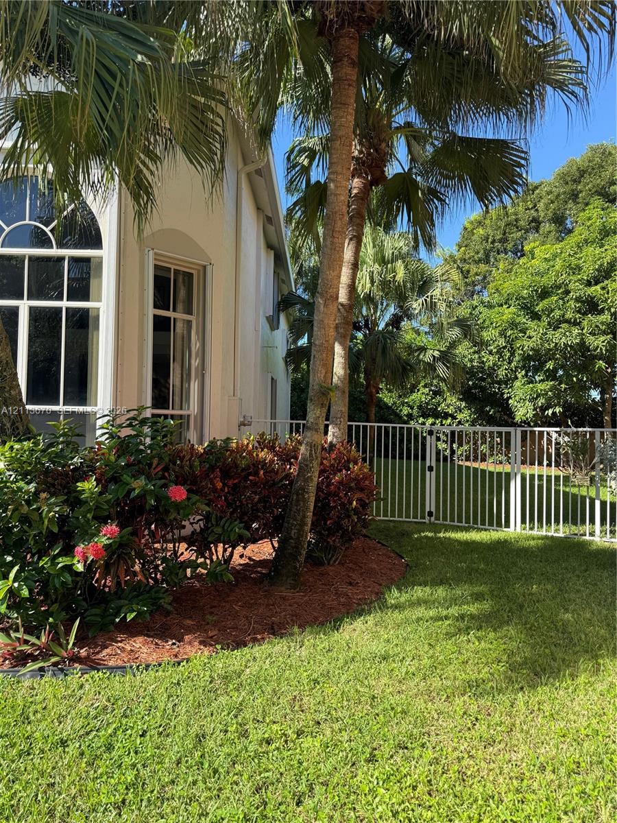 Stucco exterior featuring arched windows, mature palm trees, manicured lawn, and metal perimeter fencing Stucco exterior featuring arched windows, mature palm trees, manicured lawn, and metal perimeter fencing