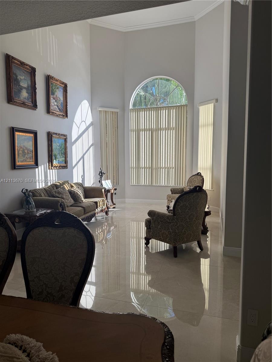 High-ceilinged living area featuring large-format polished tile flooring, an expansive arched window, and neutral wall tones High-ceilinged living area featuring large-format polished tile flooring, an expansive arched window, and neutral wall tones