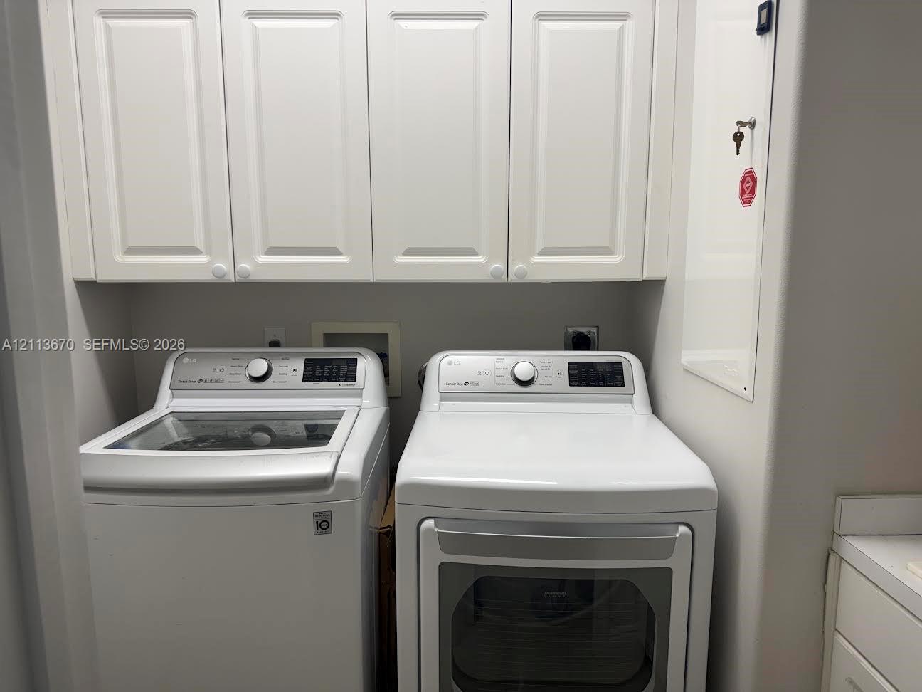 Laundry area featuring white shaker-style overhead cabinetry and built-in washing machine and dryer