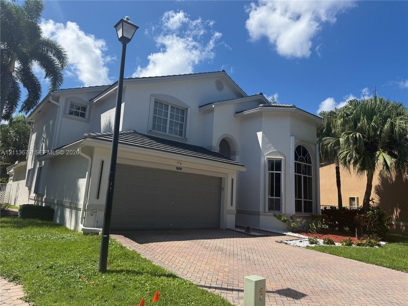 Two-story exterior featuring a light-toned stucco facade, a tile roof, an arched entryway, decorative muntin windows, and a multi-car garage with a paver driveway Two-story exterior featuring a light-toned stucco facade, a tile roof, an arched entryway, decorative muntin windows, and a multi-car garage with a paver driveway