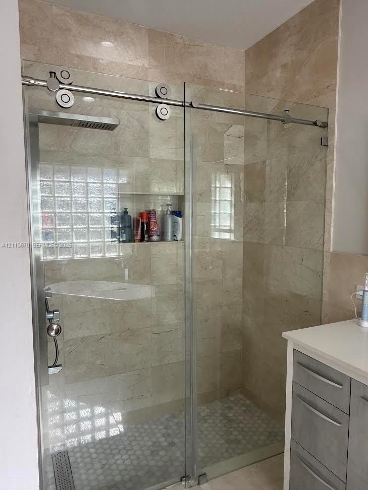 Walk-in shower featuring a sliding glass door with stainless steel hardware, floor-to-ceiling neutral tile, a built-in recessed wall niche, a rain-style showerhead, and a hexagon-tiled shower floor