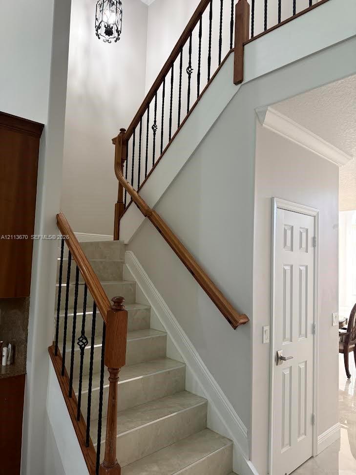 Staircase featuring stone-finish treads, wooden handrails, decorative wrought iron balusters, and a tiered metal chandelier Staircase featuring stone-finish treads, wooden handrails, decorative wrought iron balusters, and a tiered metal chandelier