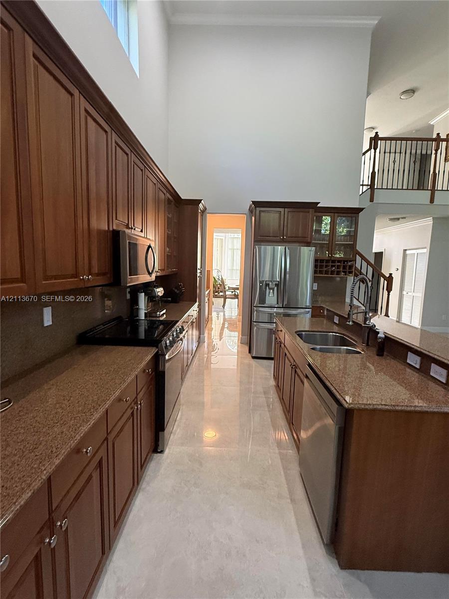 Kitchen featuring stained wood cabinetry, stone countertops, stainless steel appliances, double-basin sink, and high ceilings