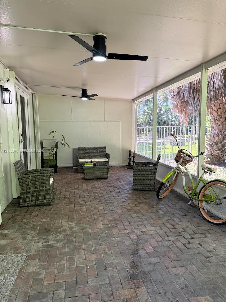 Screened-in patio featuring brick paver flooring, dual ceiling fans with integrated lighting, and metal frame wall paneling