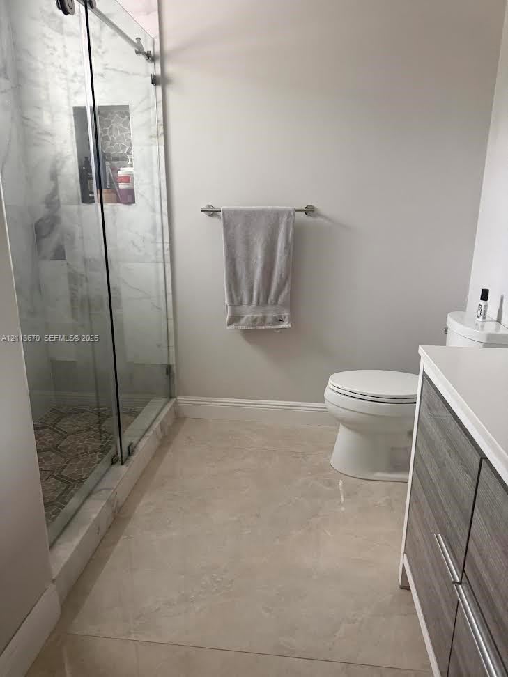 Walk-in shower with frameless glass enclosure, tiled interior, and built-in recessed niche, complemented by a vanity with wood-finish cabinetry and a solid-surface countertop