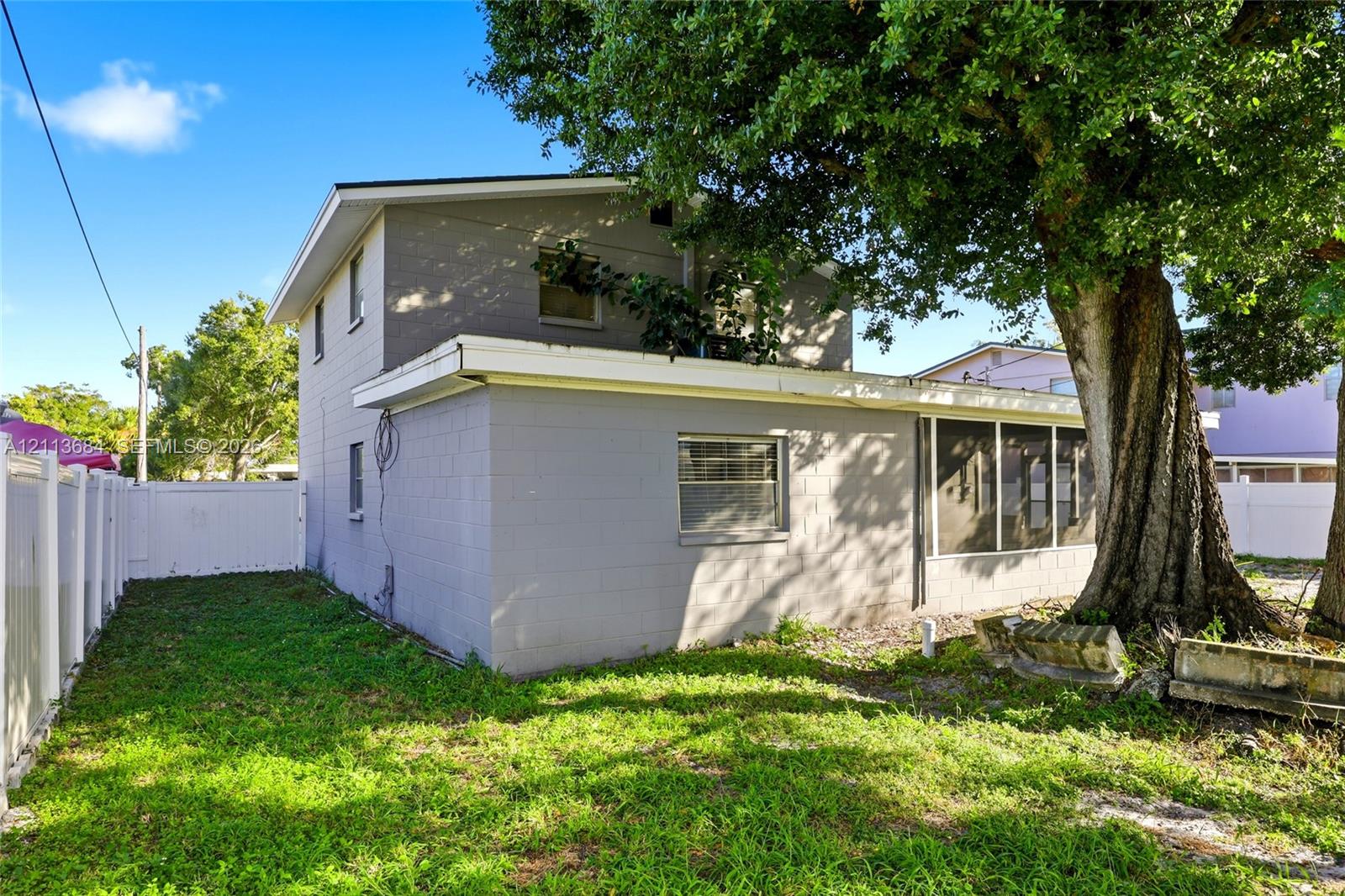 Two-story exterior featuring painted concrete block construction, a screened-in rear enclosure, and white vinyl privacy fencing