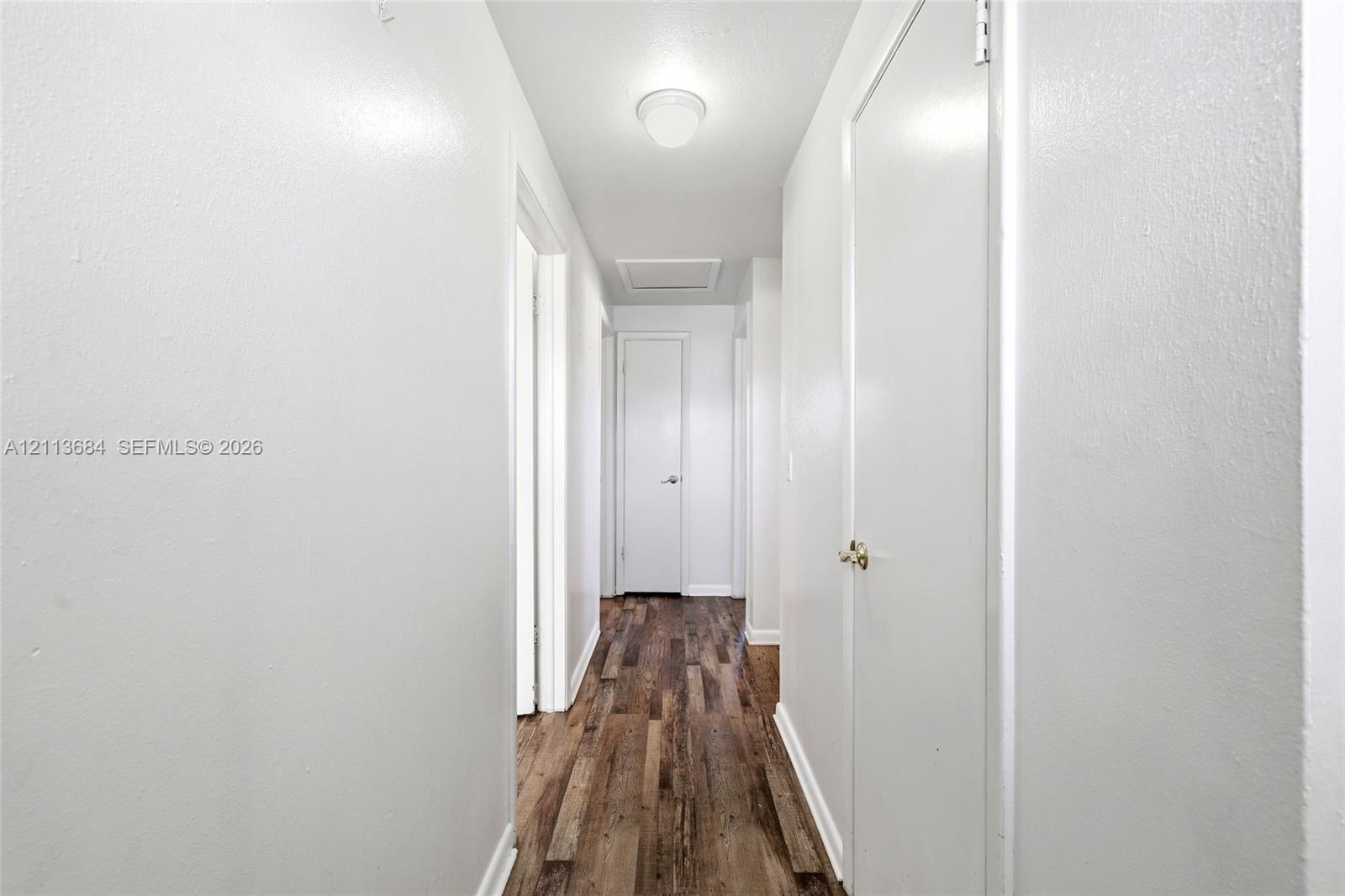Hallway featuring wood-finish flooring, crisp neutral walls, flush-mount ceiling lighting, and multiple interior doors