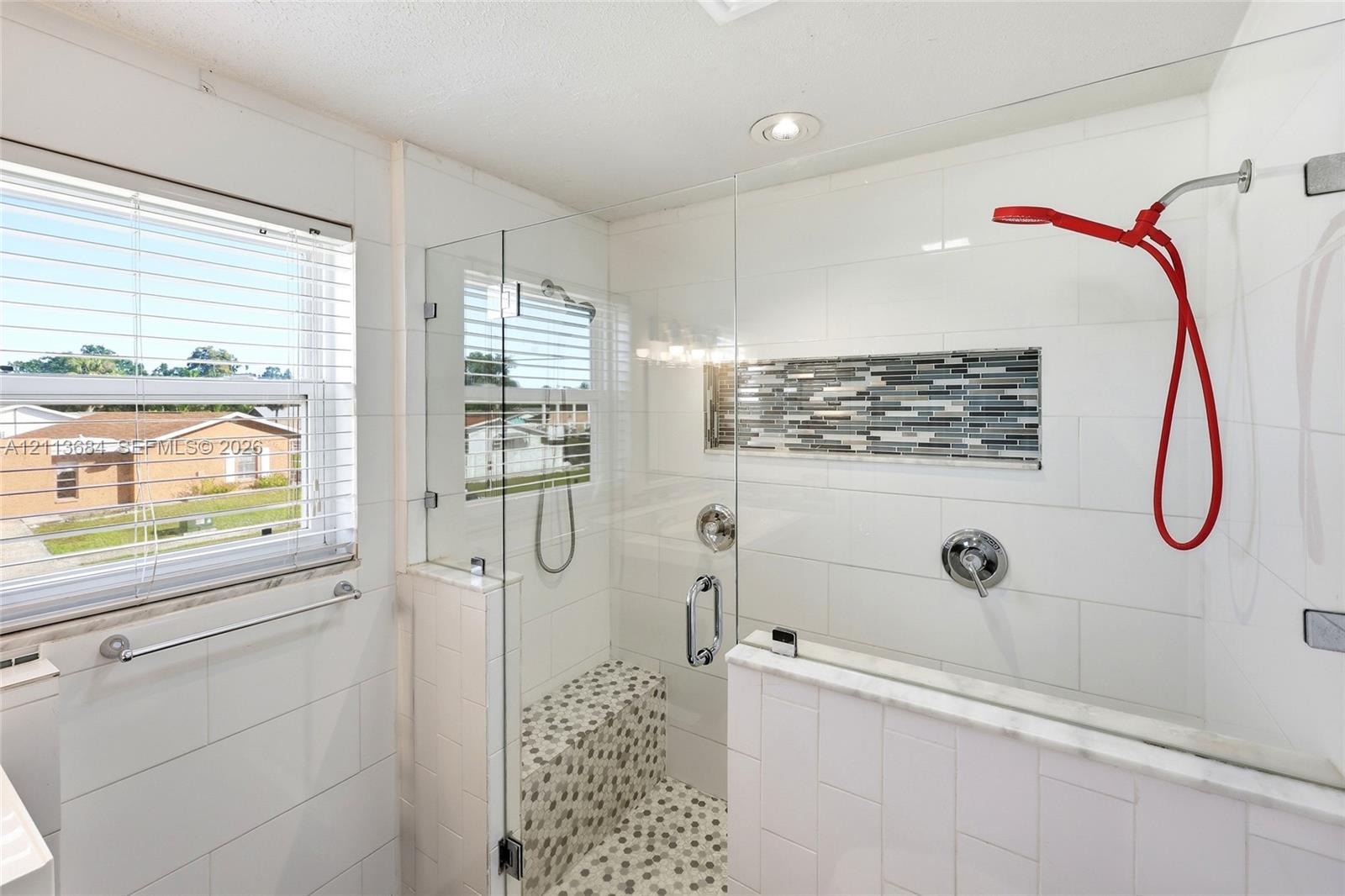Walk-in shower featuring a glass enclosure, built-in tiled bench, mosaic stone flooring, recessed decorative tile inlay, and polished chrome fixtures