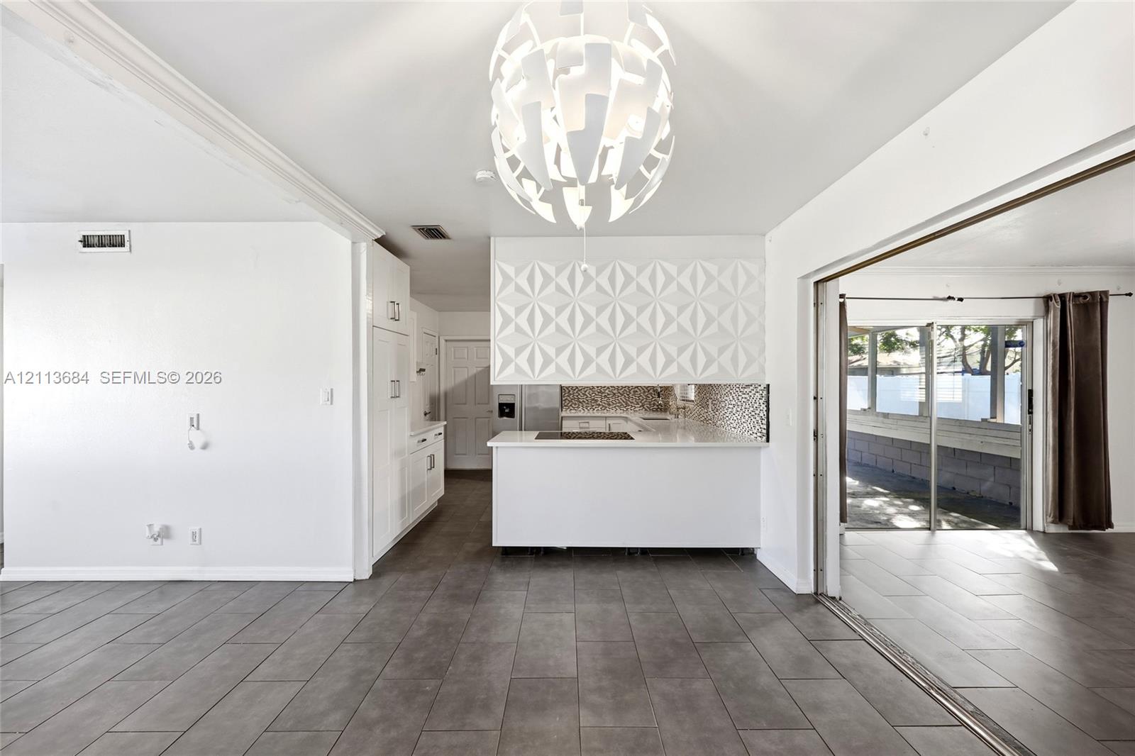Interior featuring large-format tile flooring, a geometric-patterned backsplash, a white kitchen island, and a modern tiered pendant light fixture