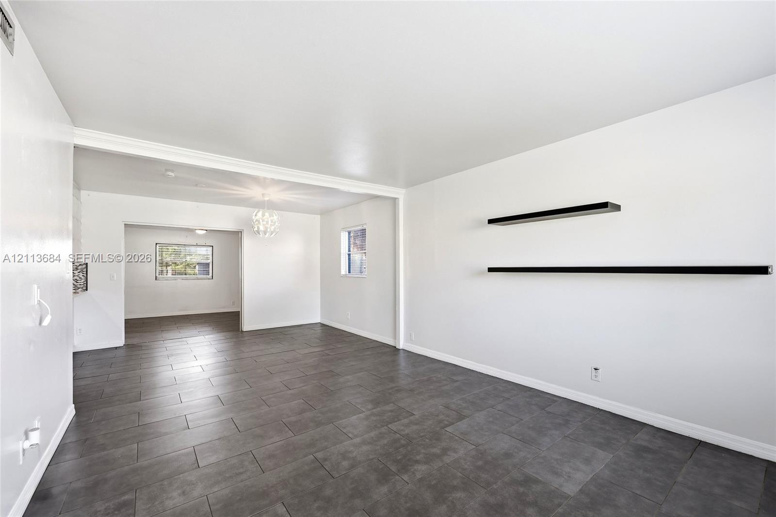 Large-format tile flooring, dual matte black floating wall shelves, and a decorative crystal-style chandelier fixture Large-format tile flooring, dual matte black floating wall shelves, and a decorative crystal-style chandelier fixture