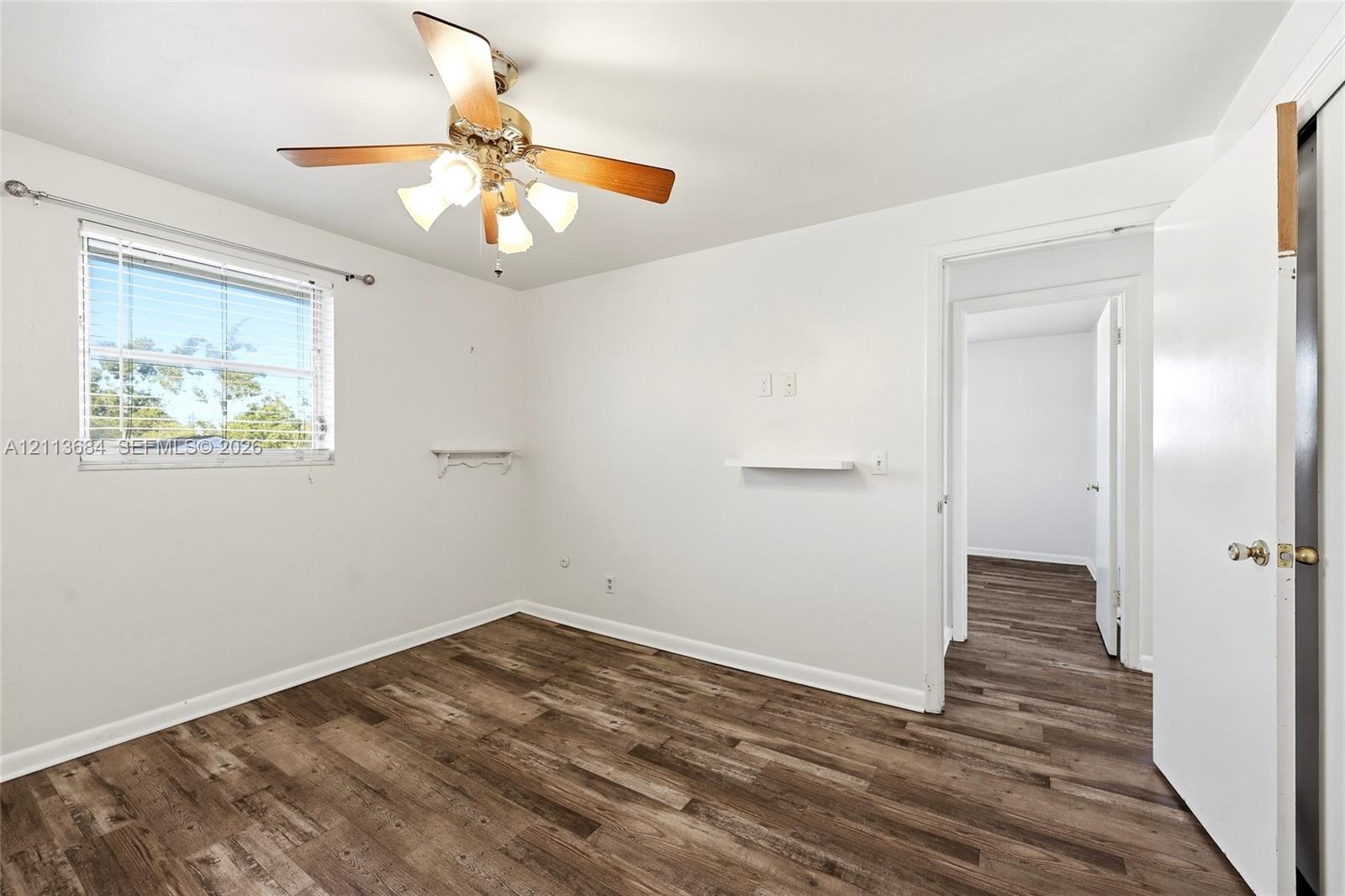 Room featuring wood-finish flooring, a multi-blade ceiling fan with integrated lighting, and a window with horizontal blinds