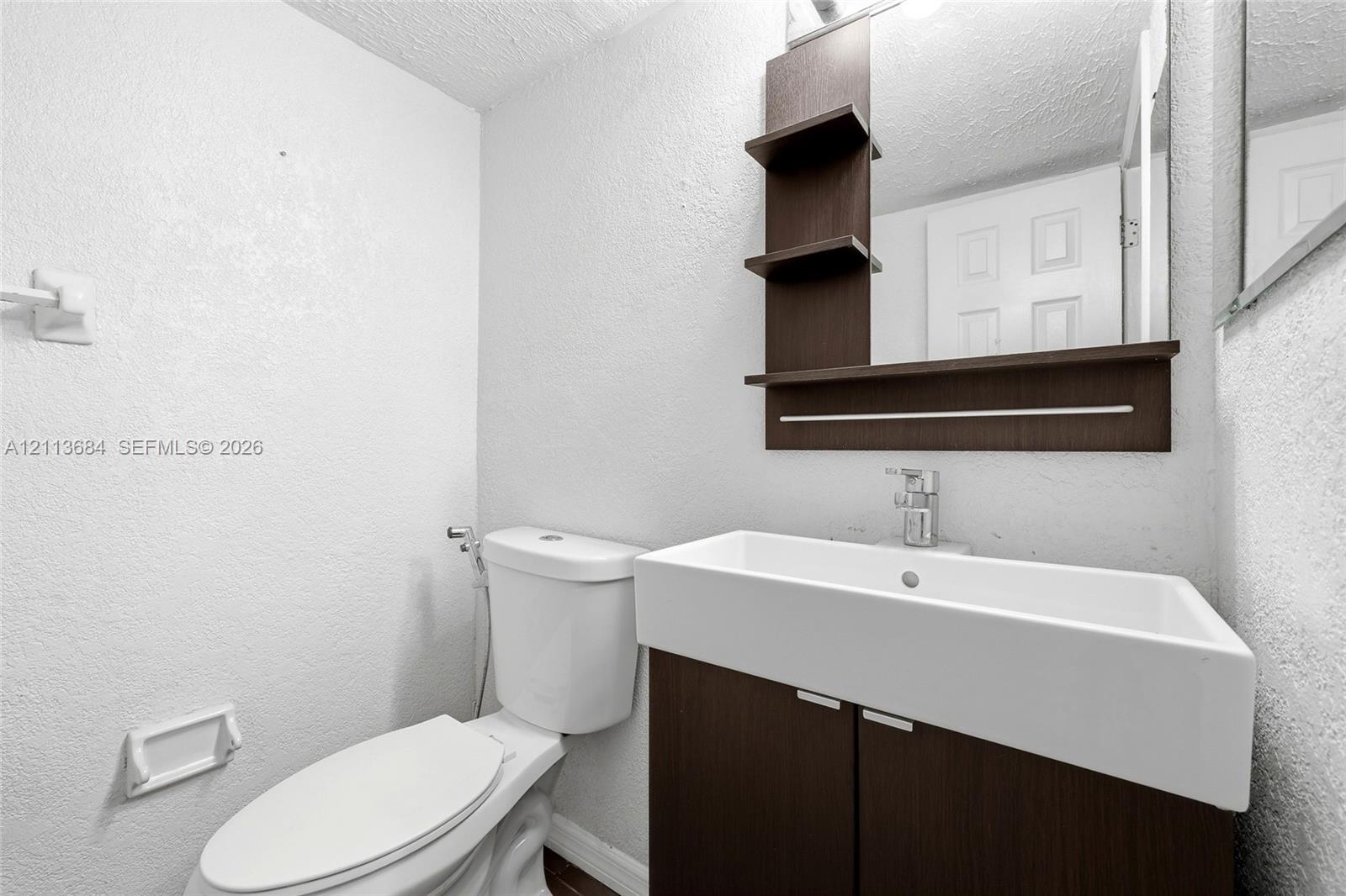 Wall-mounted vanity featuring dark wood-finish cabinetry, a rectangular vessel sink, a chrome single-handle faucet, and an integrated mirror with open shelving