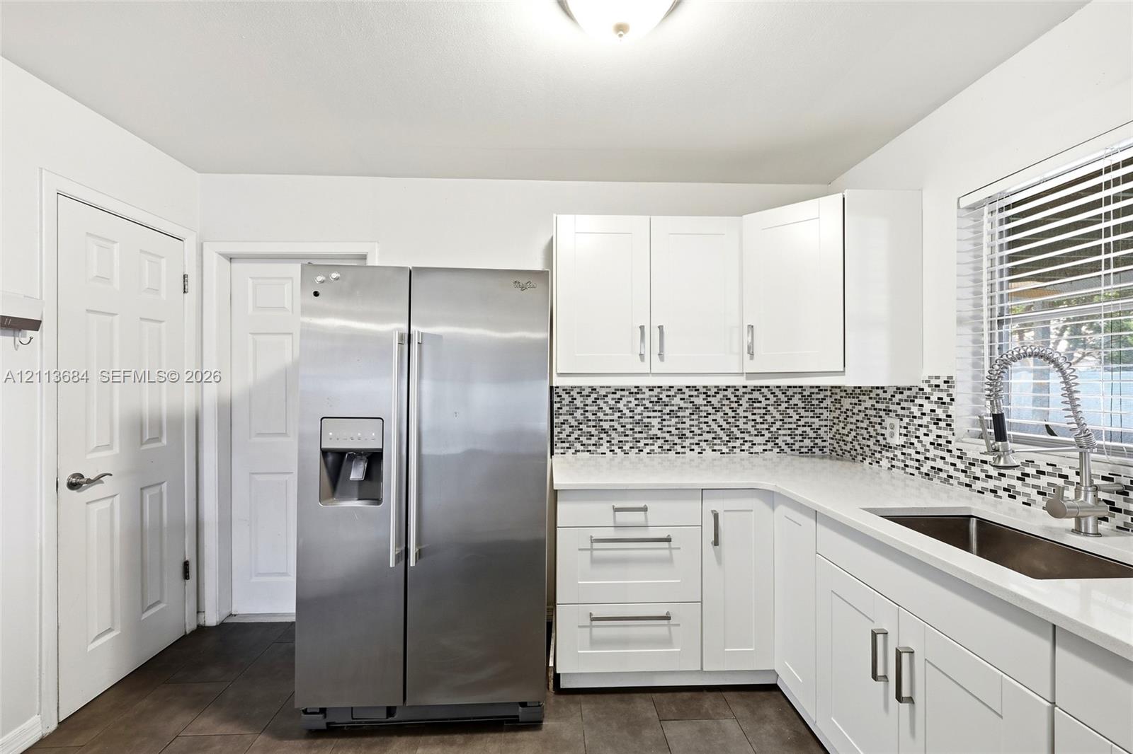 Kitchen featuring white shaker-style cabinetry, stainless steel side-by-side refrigerator, mosaic tile backsplash, solid-surface countertops, and a gooseneck kitchen faucet