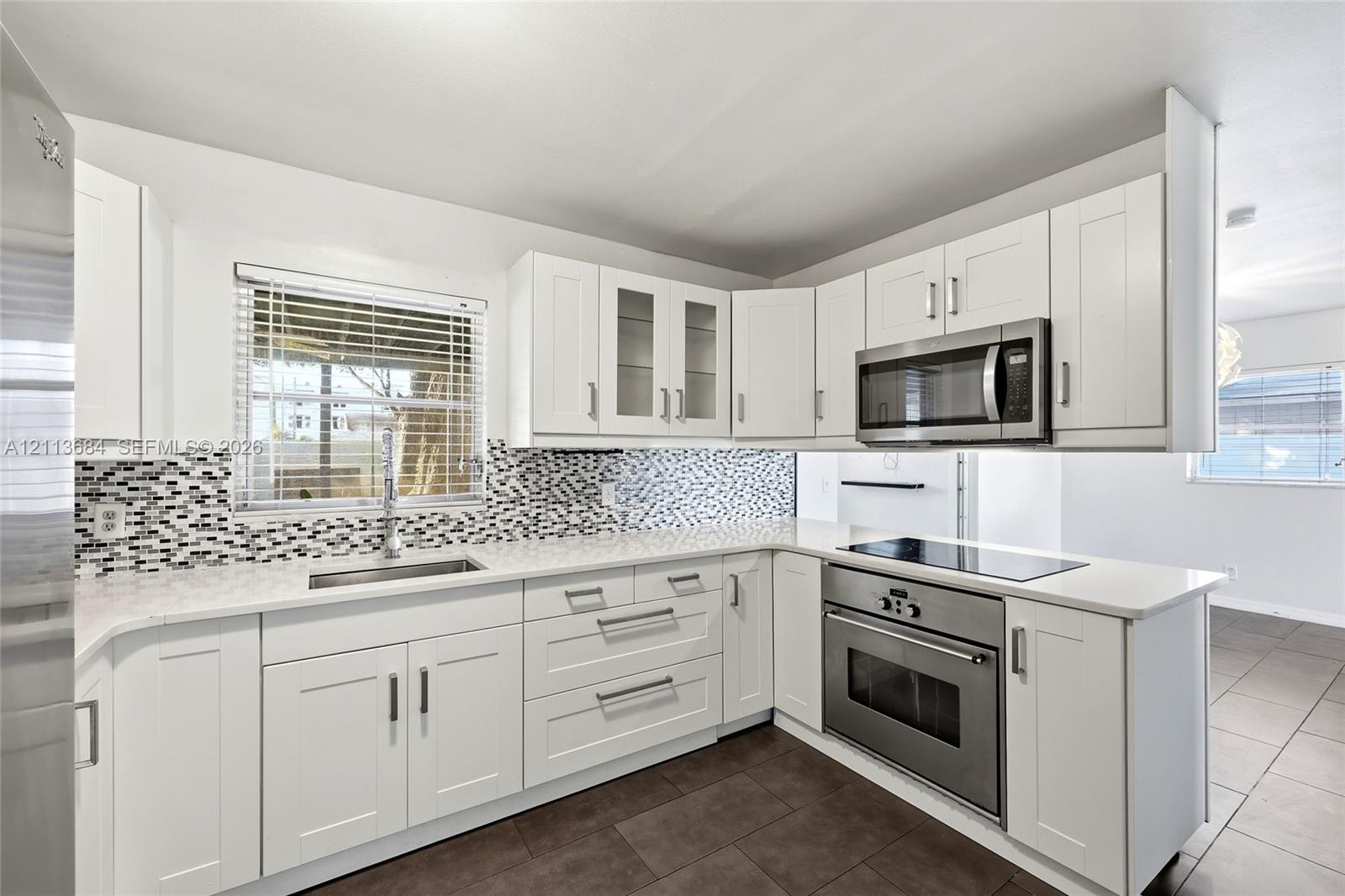 Kitchen featuring white shaker-style cabinetry, quartz countertops, a mosaic tile backsplash, stainless steel appliances, and large-format tile flooring