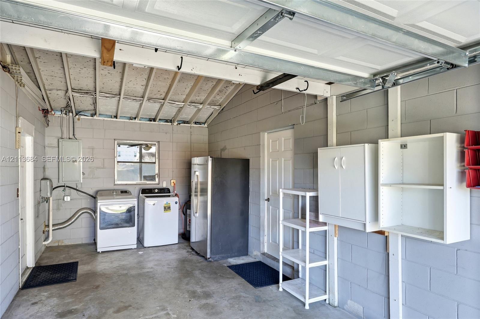 Garage featuring concrete block walls, exposed rafter ceiling, multiple wall-mounted storage cabinets, and dedicated utility hookups